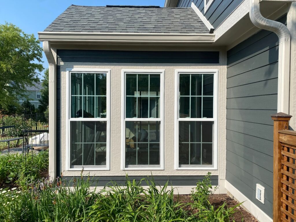 A gray home with white trim and three long vertical windows surrounded by greenery