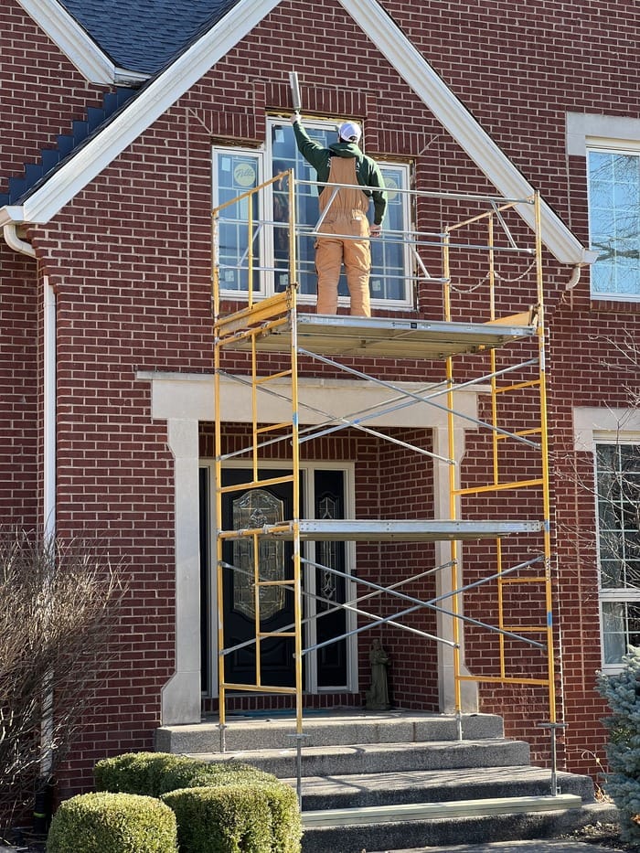 Josh Byler installing a window in a home while atop yellow scaffolding