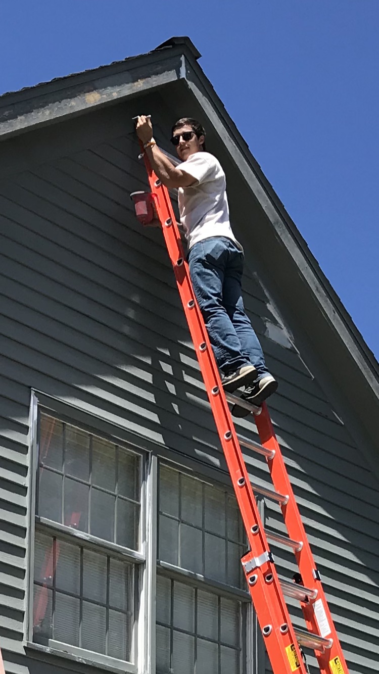 Josh Byler stands near the top of an orange ladder against a house