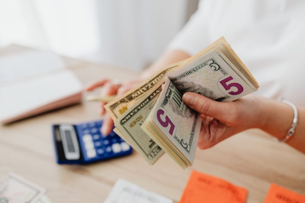 Hand holding dollars and other hand operating a calculator