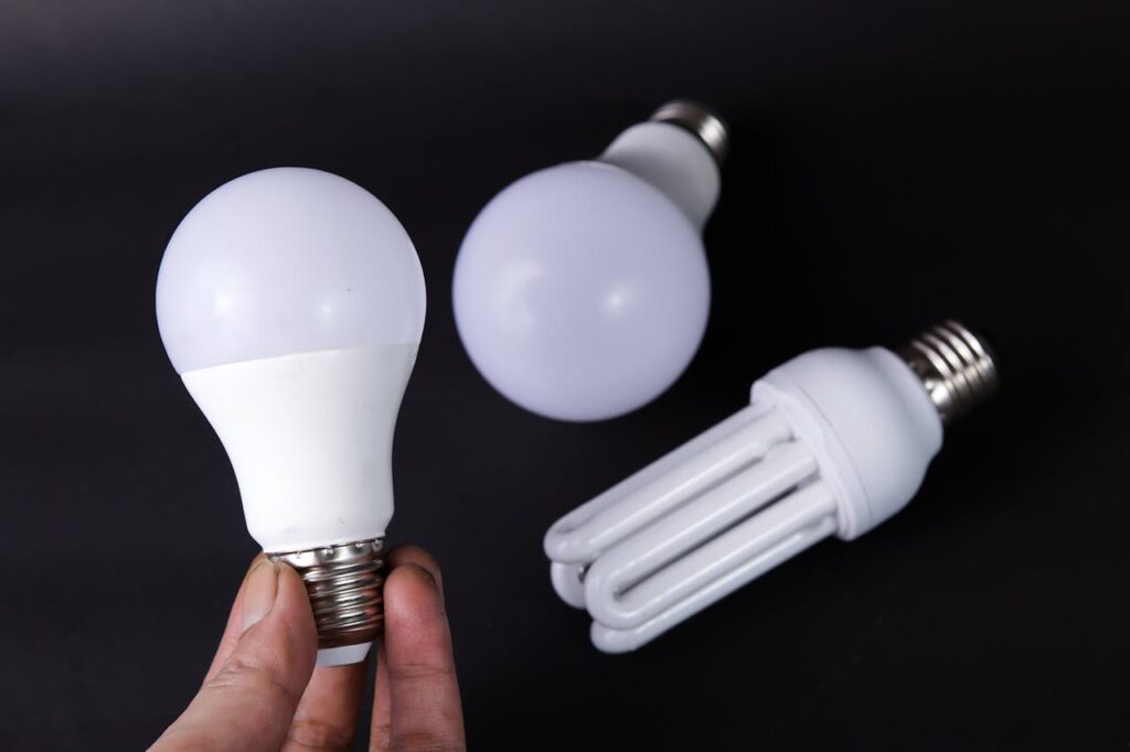 Hand holding a lightbulb with other lightbulbs on a dark background